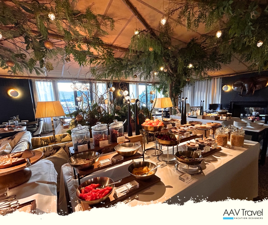 A beautifully decorated dining area featuring a variety of breakfast options, including fruit, pastries, and snacks. The atmosphere is enhanced by greenery and elegant lighting, creating a cozy and inviting setting.
