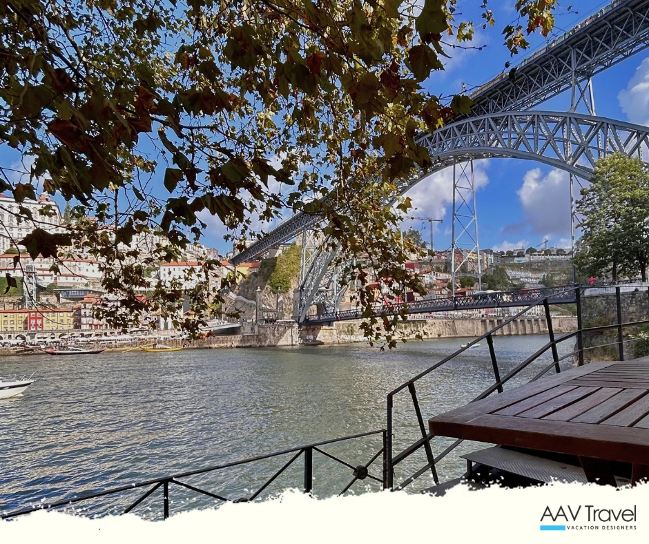 View of the Douro River with a rustic wooden table in the foreground, framed by autumn leaves, showcasing the iconic Dom Luís I Bridge in Porto, Portugal in the background.