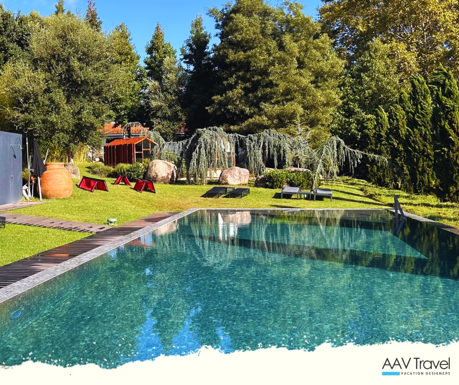 A serene outdoor pool situated in La Vinha's lush garden, surrounded by trees and a few lounge chairs, offering a tranquil escape.