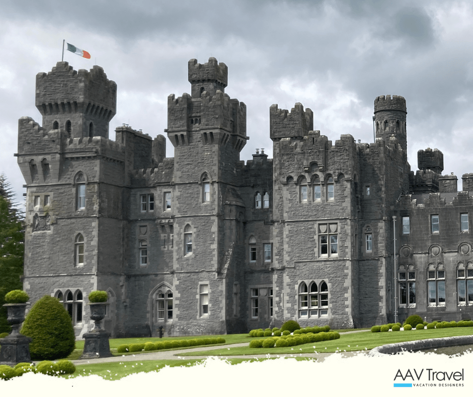 A panoramic view of Ashford Castle surrounded by lush gardens and mirrored in the still waters of Lough Corrib.